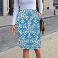 Front view of a woman standing on a city sidewalk wearing a vibrant knee-length drawstring midi skirt featuring a bold bohemian symmetrical design in orange, green, and blue, styled with a simple white top and brown purse.