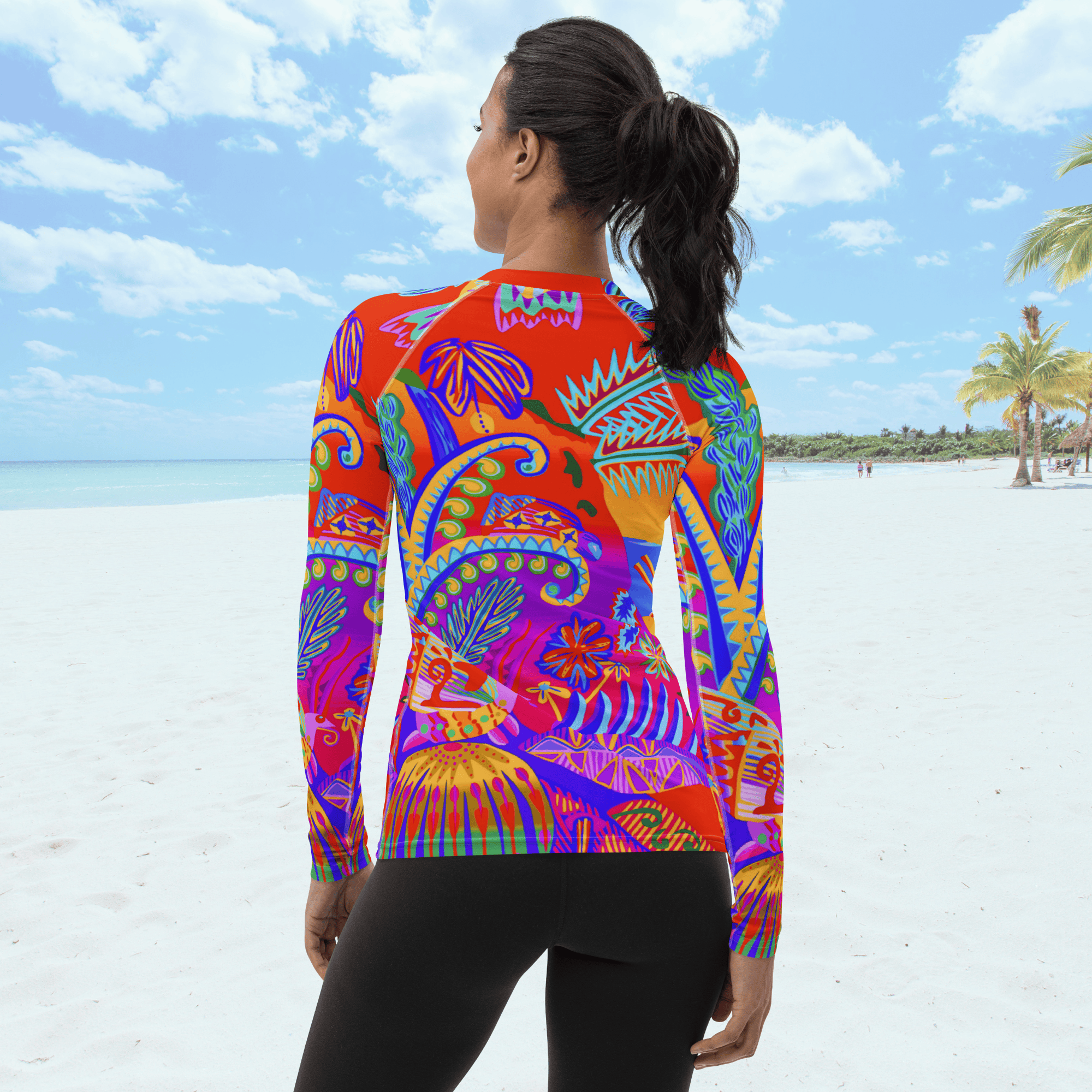 Back view of female with pony tail standing on a beach. She is wearing a a long-sleeved rash guard top with a vibrant, colorful tropical scene with insects. The top features a red base with blue, orange, purple, and yellow floral and abstract patterns.