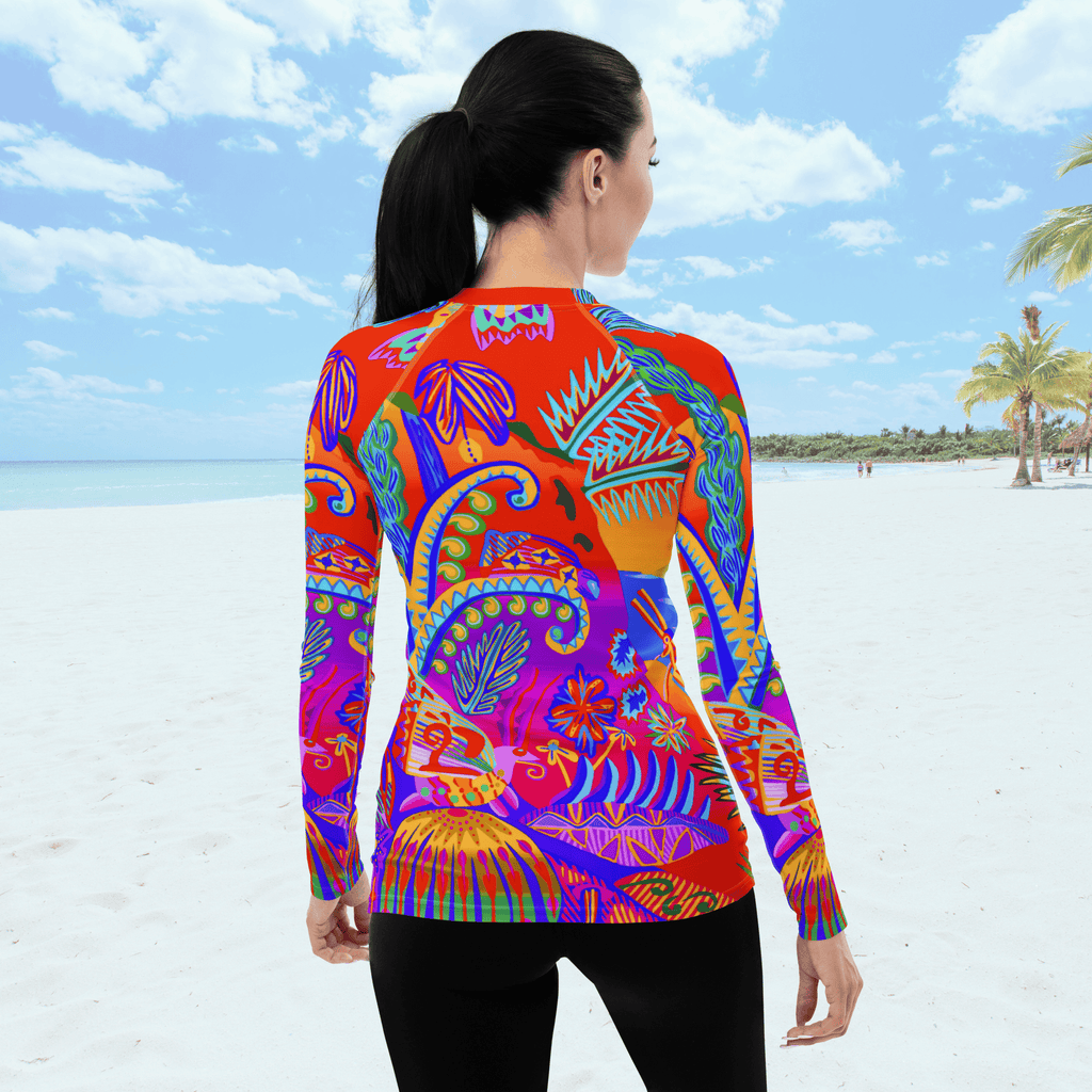 Back view of female standing on a beach. She is wearing a a long-sleeved rash guard top with a vibrant, colorful tropical scene with insects. The top features a red base with blue, orange, purple, and yellow floral and abstract patterns.