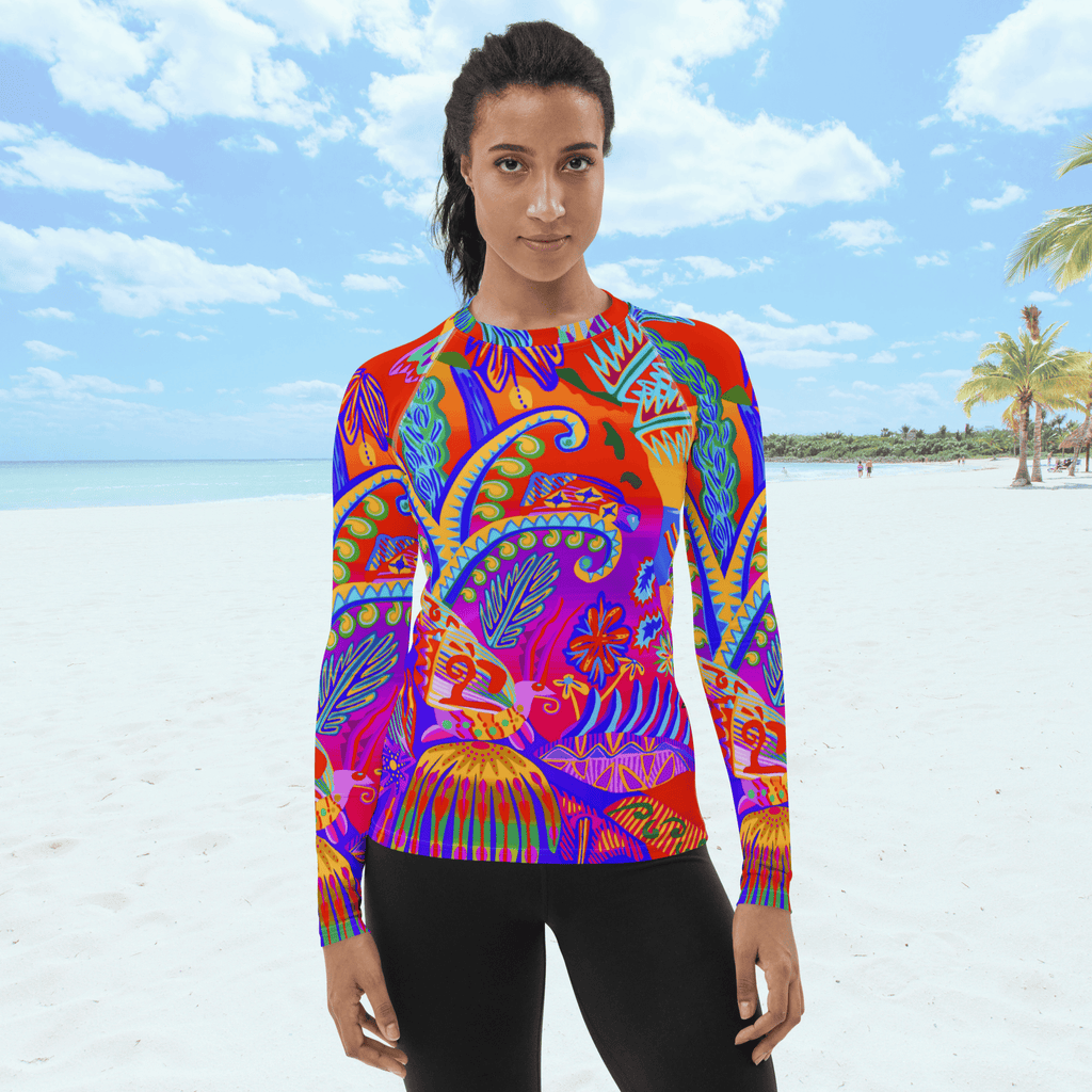 A long-sleeved rash guard top with a vibrant, colorful tropical scene with insects. The top features a red base with blue, orange, purple, and yellow floral and abstract patterns. The top is worn by a black female standing on a beach.