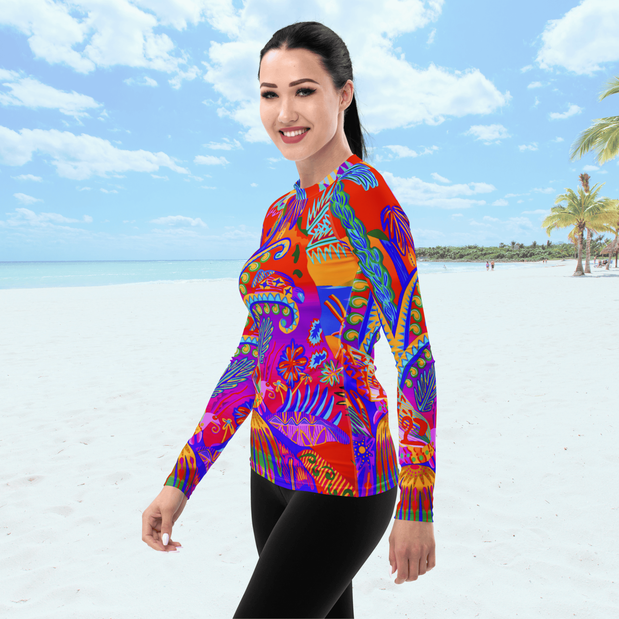Angle front view of female standing on a beach. She is wearing a a long-sleeved rash guard top with a vibrant, colorful tropical scene with insects. The top features a red base with blue, orange, purple, and yellow floral and abstract patterns.