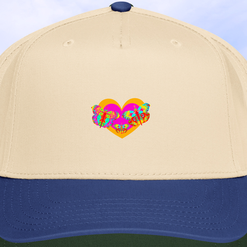 Close up of Beige cap with blue brim featuring a colorful butterfly heart design against a blurred background of buildings and trees.