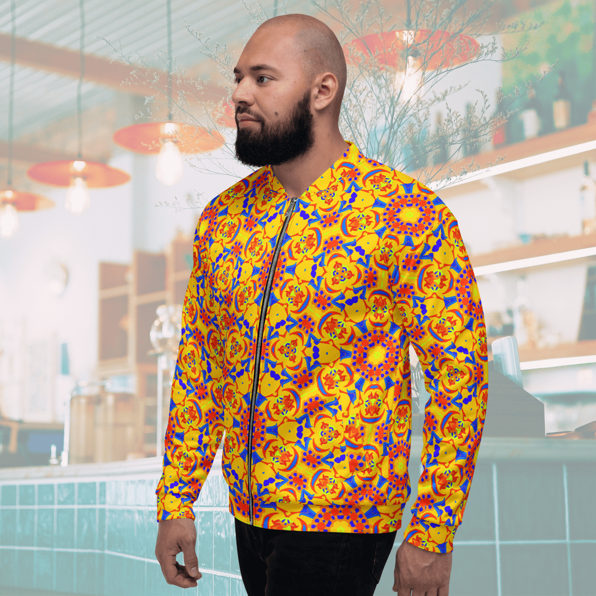 Three-quarter left side profile of a man modeling a yellow, orange, and blue abstract patterned bomber jacket in a brightly lit modern shop setting.