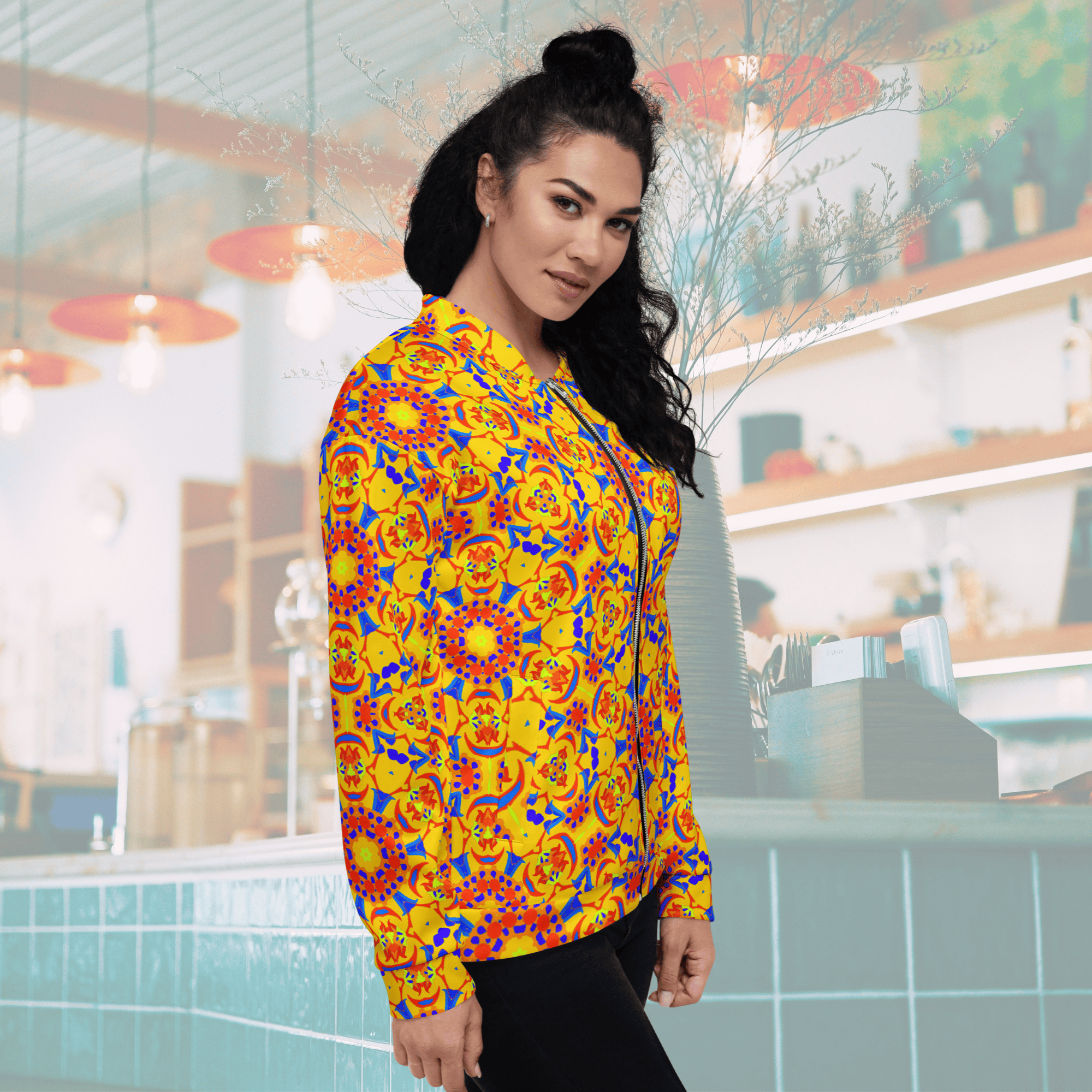 Left Side profile of a woman with her hair in a high bun wearing a yellow and orange kaleidoscope print bomber jacket with dark jeans, showing the sleek fit of the sleeve and ribbed cuff.