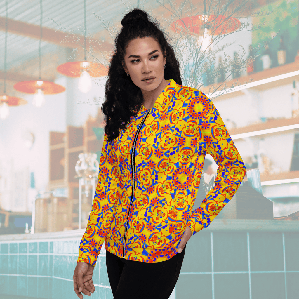 Three-quarter front view of a woman with her hand in her pocket modeling a bright yellow streetwear bomber jacket with an intricate red and blue mandala pattern.