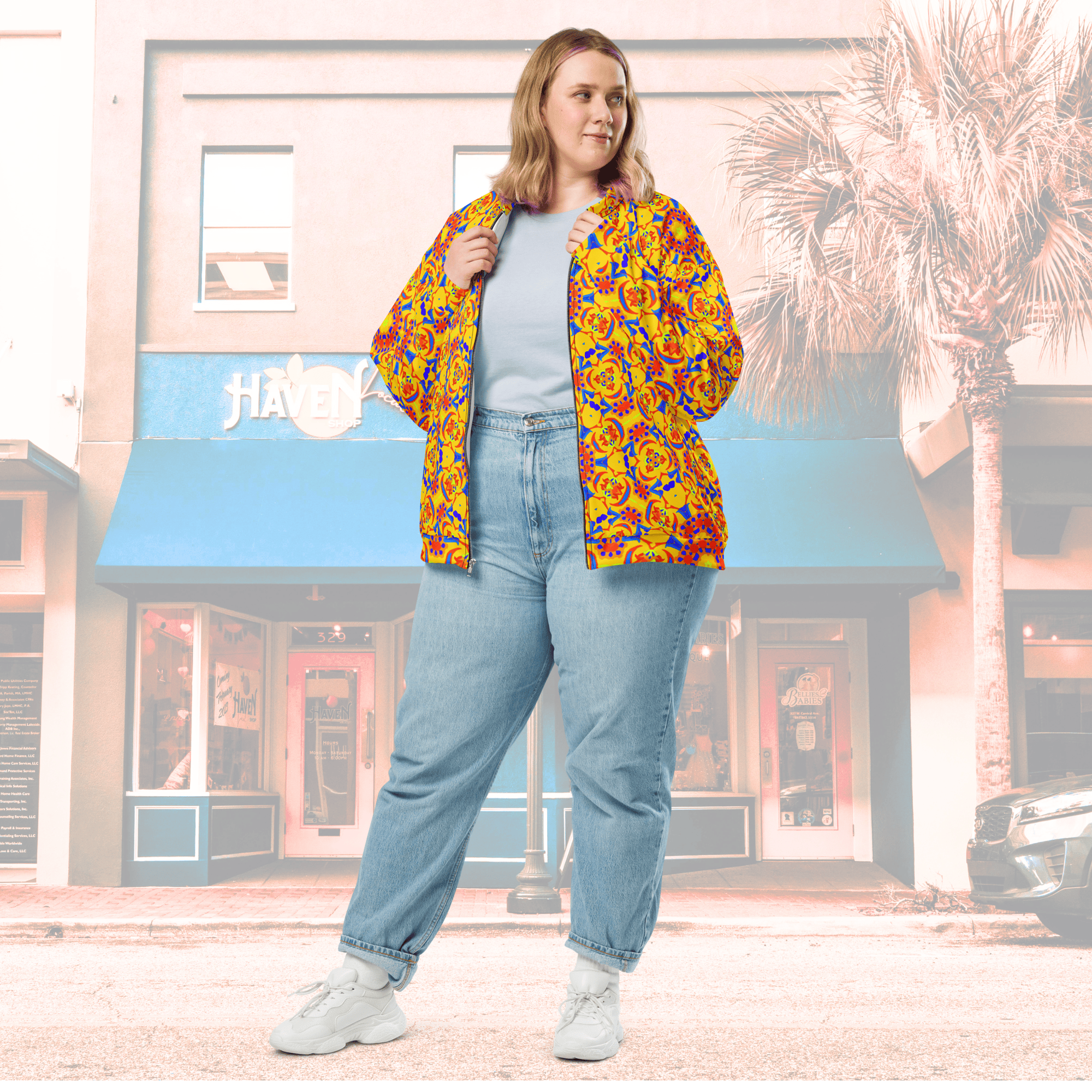 Full Frontal view of Female with Blonde Hair wearing an open Saffron Floral Yellow Unisex Bomber Jacket. She is standing outside a shopfront.