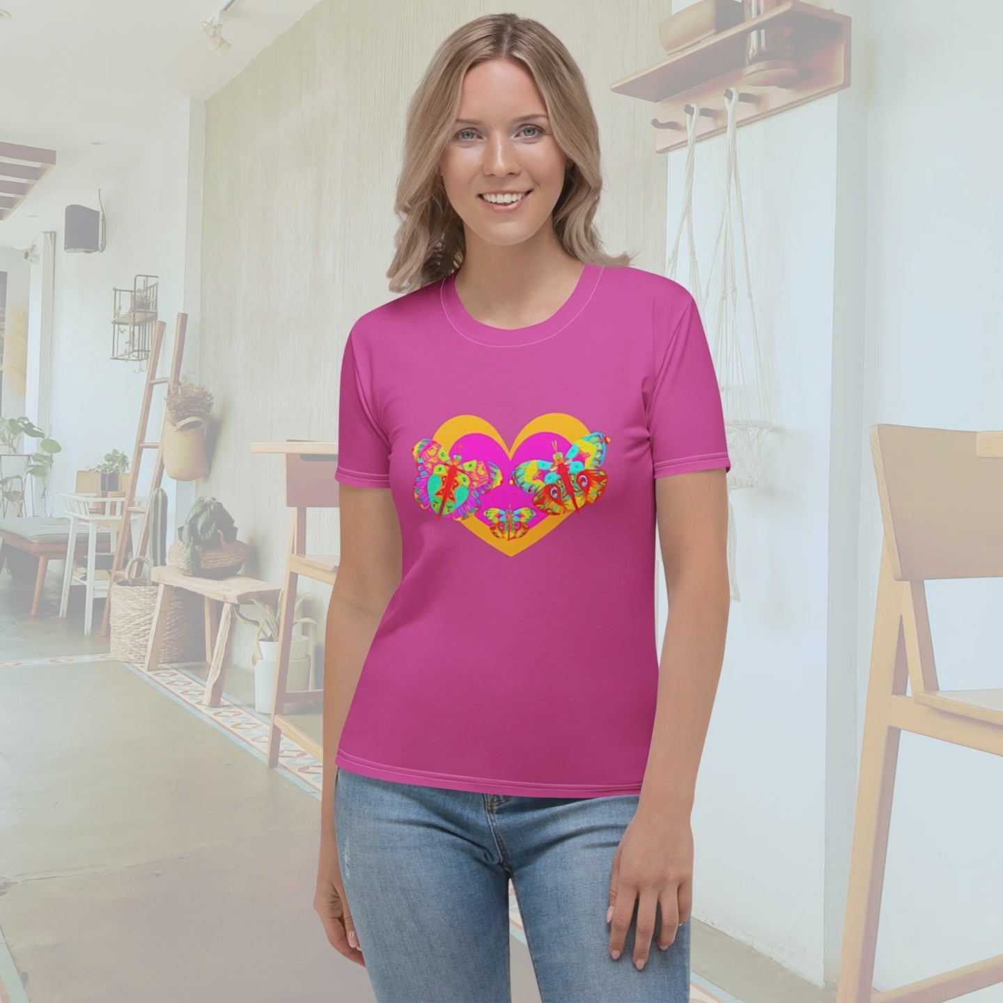 A 10-second video featuring a blonde woman modeling a pink graphic t-shirt. The video begins with a full-body shot of her standing in a cafe, followed by a smooth zoom-in on the colorful butterfly and heart design on the chest. She shifts slightly to show the garment's movement and fit before the camera pulls back to a medium shot.
